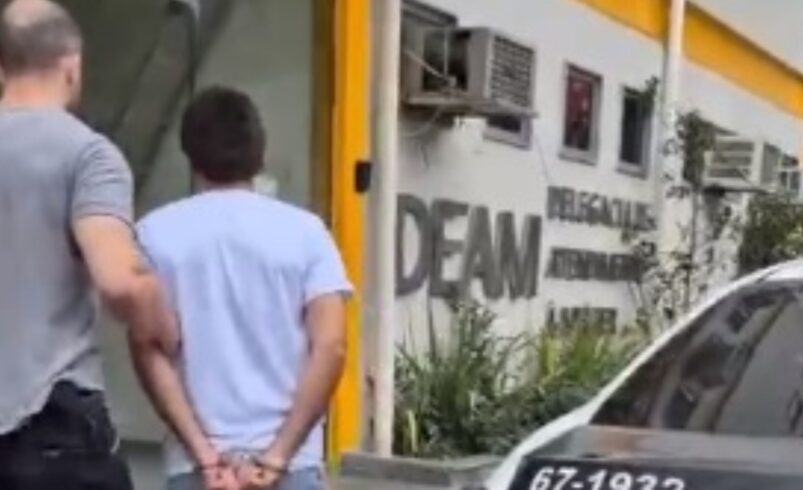 Suspeito é conduzido por policial ao interior da DEAM - NF
